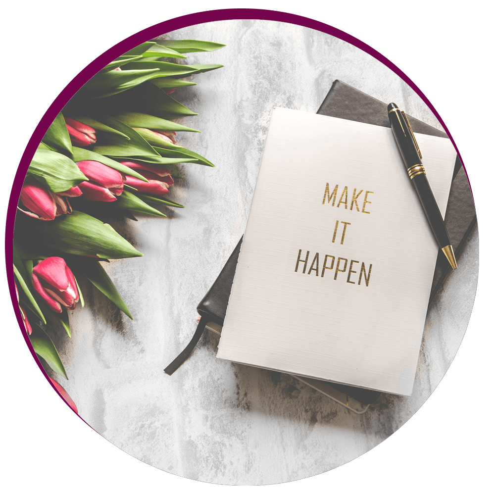 Notizbuch mit edlem Stift und einer Postkarte oben drauf mit dem Spruch "Make it happen", daneben roten Tulpen